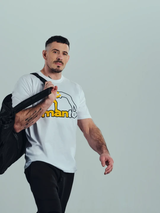 Mężczyzna w białej koszulce MANTO LOGO trzymający torbę sportową na ramieniu