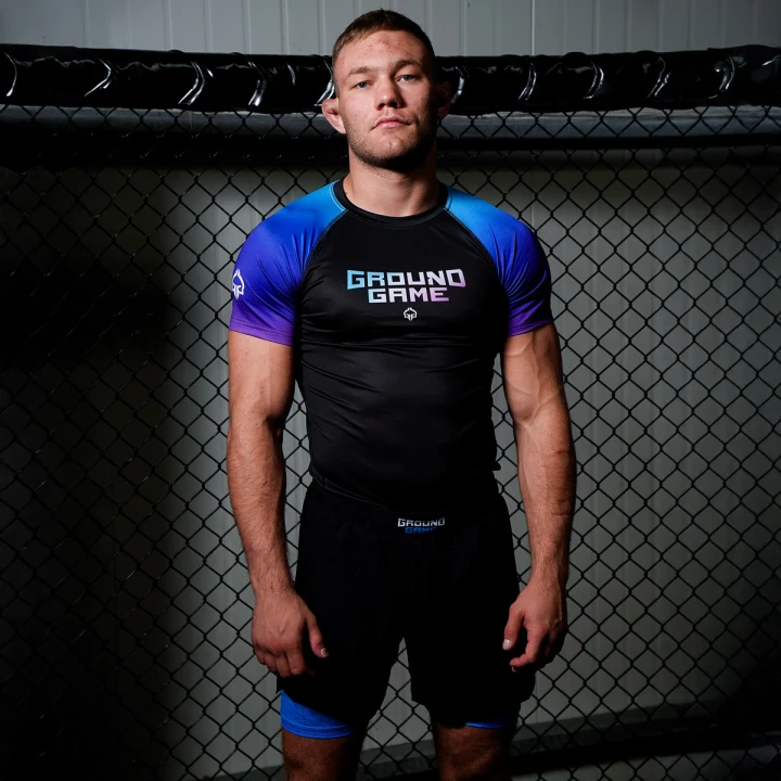 Model w stroju treningowym Ground Game z kompresyjnymi spodenkami 2w1 na tle klatki do MMA