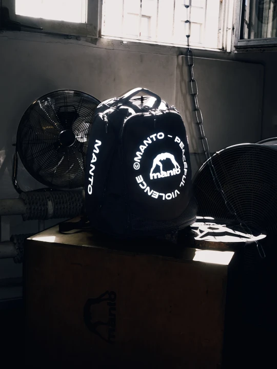Odblaskowe logo MANTO CIRCLE na czarnym plecaku sportowym po zmroku