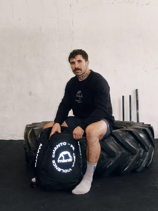 Mężczyzna siedzący z dużym plecakiem sportowym MANTO CIRCLE na sali treningowej